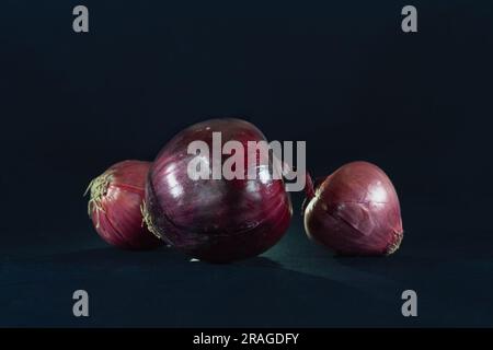 Picture of three red onions isolated on a black background. Red onions (also known as purple or blue onions in some mainland European countries) are c Stock Photo