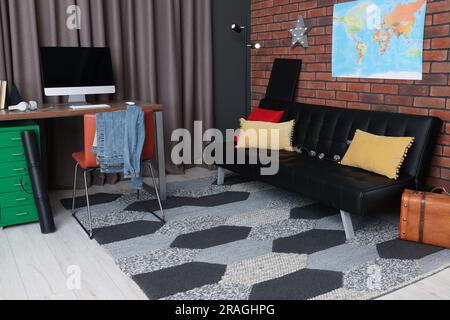 Stylish teenager's room with computer, black sofa and world map on brick wall Stock Photo