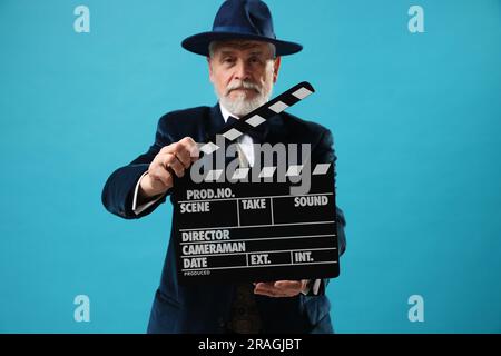 Senior actor with clapperboard on light blue background, selective focus. Film industry Stock Photo