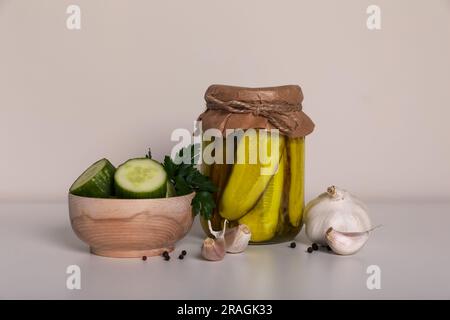 Tasty pickled cucumbers, cut vegetables in wooden bowl and garlic on white table Stock Photo