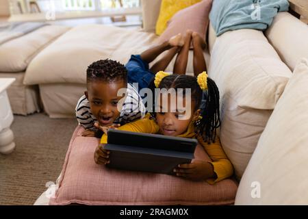 High angle view of african american siblings using digital tablet while lying on sofa in living room Stock Photo