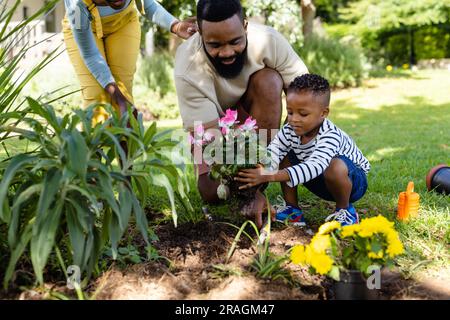 African american woman standing by father and son planting fresh flowers in field at yard Stock Photo