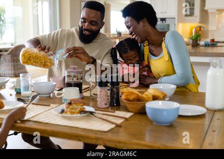 African american parents and daughter laughing cheerfully and having breakfast at dining table Stock Photo