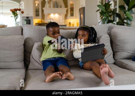African american siblings using digital tablet and mobile phone while sitting on sofa in living room Stock Photo