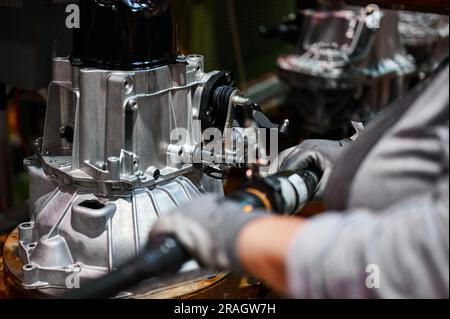 Worker connects car engine gearbox details on shop conveyor Stock Photo