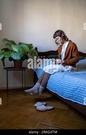 Sad teen girl sitting on bed with smartphone Stock Photo