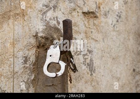 iron handcuffs hanging on a hook on the wall of the house close-up Stock Photo