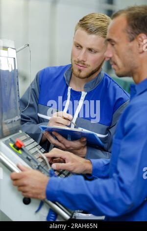 portrait of two men wearing overalls operating modern machines Stock Photo