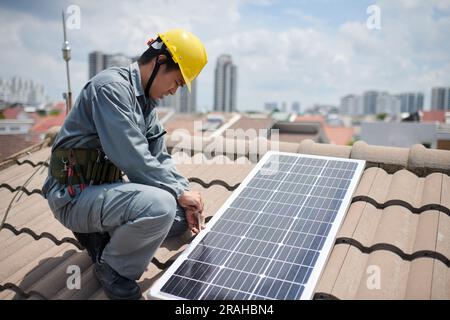 Worker in uniform and hardhat screwing solar panel on roof Stock Photo