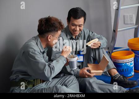 Builders eating instant noodles and sandwiches for lunch at construction site Stock Photo