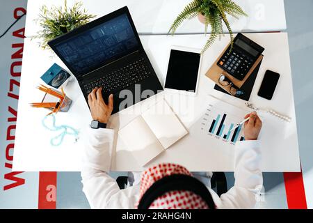 Unrecognizable arab businessman in traditional outfit working at the table in office Stock Photo