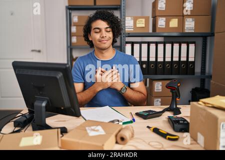Hispanic man with curly hair working at small business ecommerce smiling with hands on chest with closed eyes and grateful gesture on face. health con Stock Photo