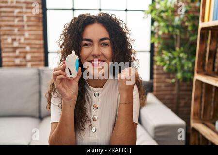 Young hispanic woman using glucose meter screaming proud, celebrating victory and success very excited with raised arms Stock Photo