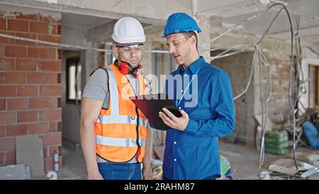 Two men builder and architect writing document speaking at construction site Stock Photo