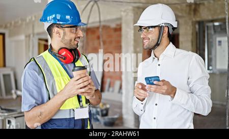 Two men builder and architect using smartphone drinking coffee at construction site Stock Photo