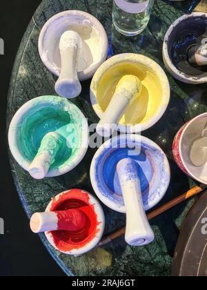 Cups and bowls used as color pots plus well worn brushes standing on a rock table used to paint pottery. Stock Photo