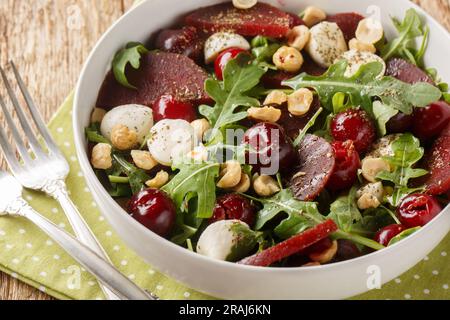 Homemade arugula salad, baked beets, ripe cherries, mozzarella, hazelnuts close-up in a bowl on the table. Horizontal Stock Photo