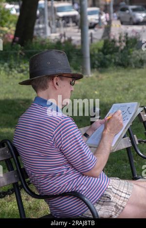 Doing the New York Times daily crossword puzzle on a bench in Washington Square Park in lower Manhattan. Stock Photo