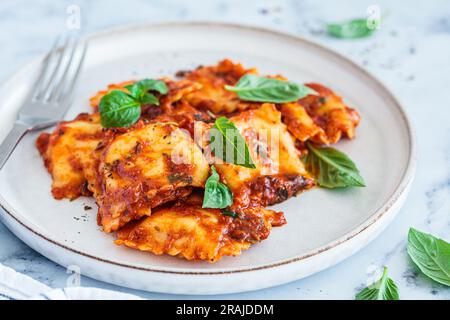 Ravioli with ricotta, tomato sauce and basil, white marble background, close-up. Stock Photo