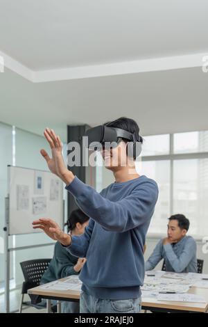 A cheerful and excited young Asian male developer tested a new VR game on a VR headset in the meeting with team. Virtual reality Stock Photo