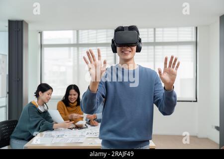 A cheerful and excited young Asian male developer tested a new VR game on a VR headset in the meeting with team. Virtual reality Stock Photo