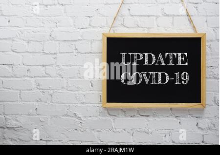 Update Covid-19 typography text on wooden blackboard hanging on white brick wall background Stock Photo