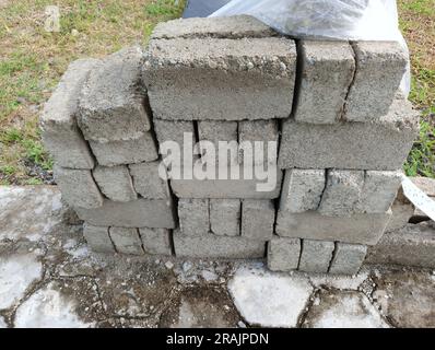 Stacked concrete building blocks on a hexagonal paving stone surface in an outdoor yard. Construction materials for masonry . Stock Photo