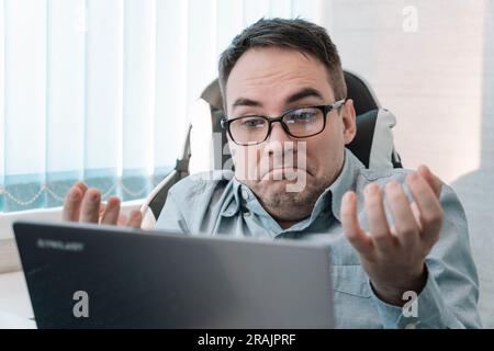 male employee in a blue jacket works with documents and on a computer in a bright office. Surprised emotion on the face. Stock Photo