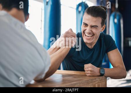 Strong, active and men arm wrestling in the gym on a table while being playful for a challenge. Rivalry, game and male people or athletes doing Stock Photo