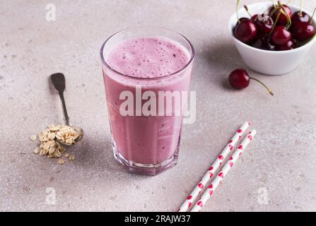 Milkshake with cherries, yogurt and oatmeal, drinking straws, bowl with fresh cherries on a beige textured background. Stock Photo