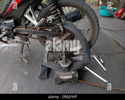 A motorcycle whose rear tire is being punctured and patched with traditional tire patching equipment in a repair shop. Stock Photo