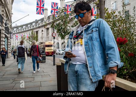 London- June 2023: A man looking at his smart phone on Regent Street, landmark shopping destination in the West End Stock Photo