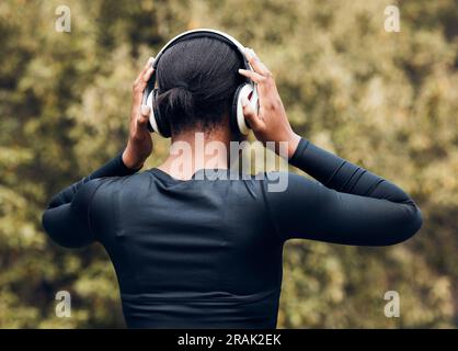 Fitness, back view of woman in woods and with headphones listening to music for workout. Exercise or committed, training or focused and female athlete Stock Photo