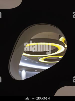 Looking through the Glass mirrored wall panels in the living room can see the hanging rounded ceiling mounted light fixtures with modern LED light bul Stock Photo