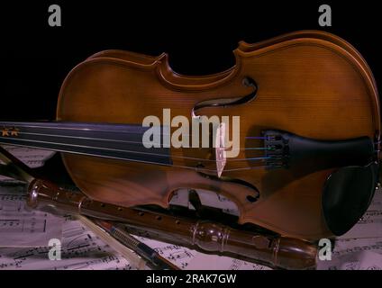 Violin with bow and recorder on music sheets Stock Photo