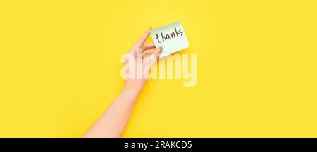 Female hand holding sticky note with word THANKS on yellow background Stock Photo