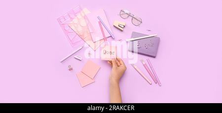 Female hand holding sticky note with word DONE and stationery on lilac background Stock Photo