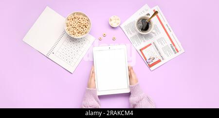 Female hands holding tablet computer, calendar, newspaper and breakfast on lilac background Stock Photo