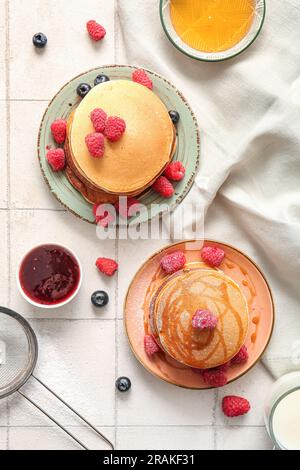 Plates of tasty pancakes with raspberries and blueberries on white tile background Stock Photo