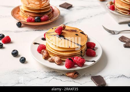 Plates of tasty pancakes with raspberries, blueberries and nuts on white marble background Stock Photo