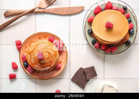 Plates of tasty pancakes with raspberries and blueberries on white tile background Stock Photo