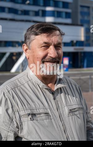 Portrait of a gray-haired 70-year-old man with a beard and mustache. A confident man smiles while looking at the camera. Stock Photo
