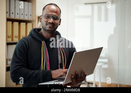 Portrait of cheerful software developer with laptop sta nding in office of IT company Stock Photo