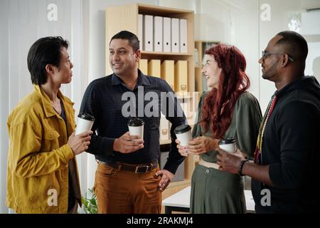 Friendly cheerful colleagues drinking coffee and discussing weekend in office Stock Photo