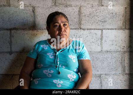 Ahuachapán, El Salvador - November 04 2022: Salvadoran Woman Sitting Outside her House Against a Backdrop of Gray Bricks Stock Photo