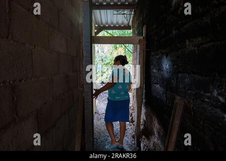 Ahuachapán, El Salvador - November 04 2022: Salvadoran Woman Dressed in Aqua Walks Down a Narrow Adobe Hallway Stock Photo