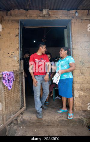Ahuachapán, El Salvador - November 04 2022: A Salvadoran Woman Stands Happily with her Son at the Enter of a Rustic Adobe House Stock Photo