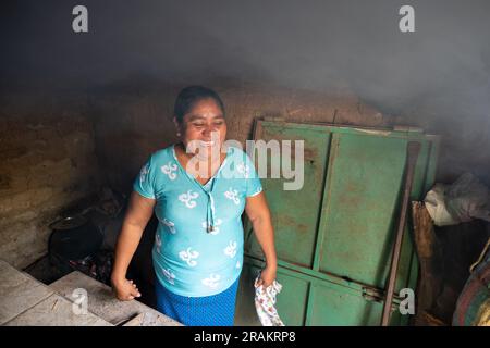 Ahuachapán, El Salvador - November 04 2022: A Salvadoran Woman is in the Kitchen Laughing as Smoke Rises from the Stove Stock Photo