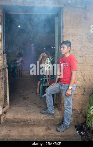 Ahuachapán, El Salvador - November 04 2022: A Salvadoran Young Man Stands Happily at the Enter of a Rustic Adobe House Stock Photo