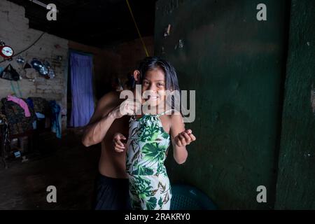 Ahuachapán, El Salvador - November 04 2022: Little Salvadoran Girl Smiling and Looking at the Camera While her Brother Helps her Get Dressed Stock Photo